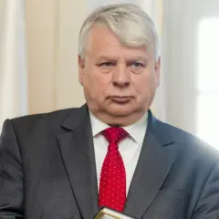 Bogdan Borusewicz w garniturze i czerwonym krawacie, na tle flagi Polski.