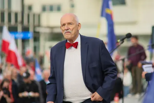 Janusz Korwin-Mikke w muszce, na tle tłumu i flag. Czy to prawica czy lewica, jego styl jest niepowtarzalny.