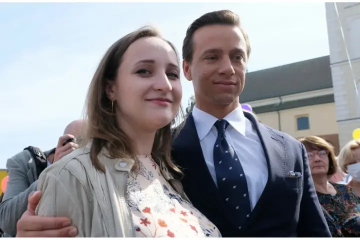 Młoda kobieta uśmiecha się, stojąc obok mężczyzny w garniturze. To żona Bosaka, która towarzyszy mu w ważnych wydarzeniach.