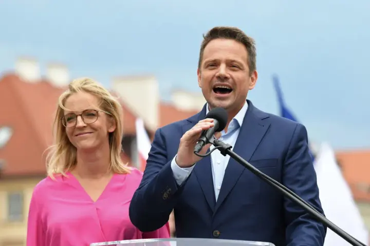 Rafał Trzaskowski przemawia, obok niego stoi jego żona, Małgorzata Trzaskowska, w różowej bluzce.