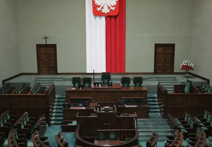 Pusta sala sejmowa z rzędami zielonych foteli i mównicą. Biało-czerwona flaga i godło Polski. Zastanawiasz się, ile jest posłów w sejmie?
