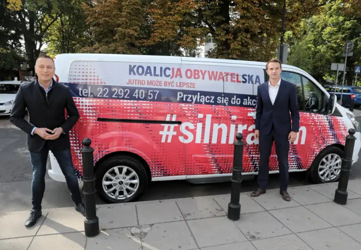Dwóch mężczyzn stoi obok vana z napisem "Koalicja Obywatelska" i hasłem "#silnirazem".