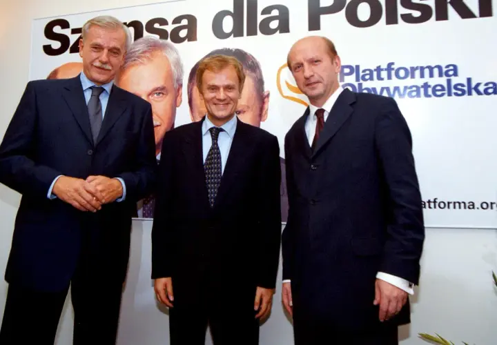 Trzech mężczyzn w garniturach, założyciele Platformy Obywatelskiej, pozuje na tle banera z napisem "Szansa dla Polski".