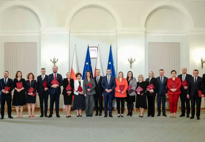 Grupa osób w eleganckich strojach, z flagami Polski w tle. Czy wśród nich jest premier Polski?