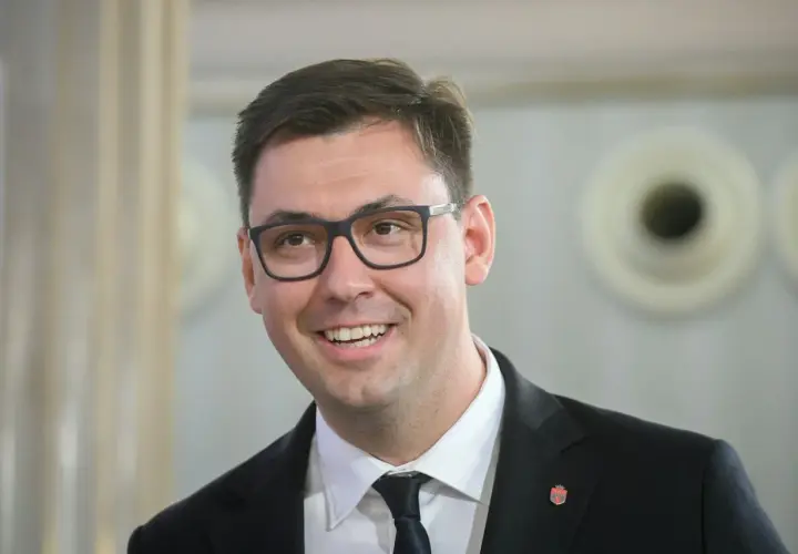 Uśmiechnięty Konrad Frysztak w okularach, w garniturze. Jego wykształcenie pozwala mu na pewność siebie w każdej sytuacji.