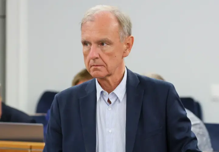 Portret starszego mężczyzny w granatowej marynarce i pasiastym jasnym koszuli.