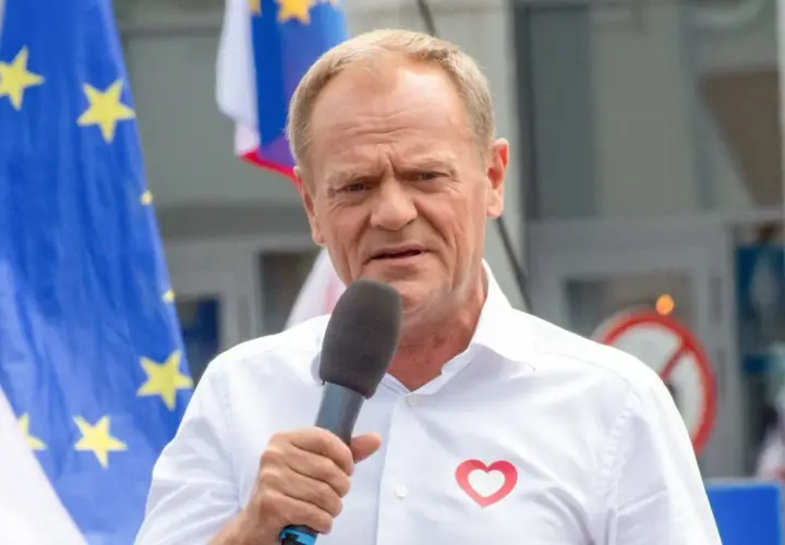 Donald Tusk przemawia w Ostródzie, z flagą UE i sercem na koszuli.