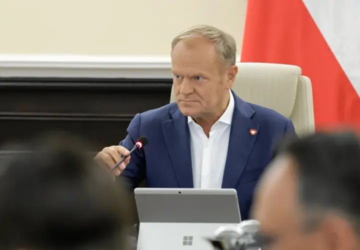 Donald Tusk w Płocku podczas spotkania. Siedzi przy stole z mikrofonem i laptopem.