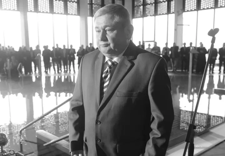 Jan Harhaj, starosta lidzbarski, w garniturze, stoi przed grupą ludzi w jasnym pomieszczeniu.