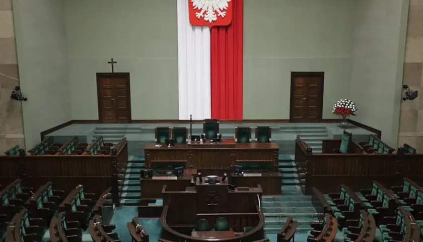 Pusta sala sejmowa z rzędami zielonych foteli i mównicą. Biało-czerwona flaga i godło Polski. Zastanawiasz się, ile jest posłów w sejmie?