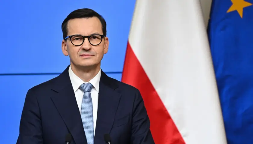 Mateusz Morawiecki w okularach, obok flagi Polski i UE. Jego rządzenie trwa od 2017 roku, kiedy to zastąpił Beatę Szydło.
