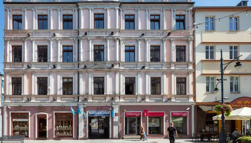 Kamienica przy ul. Piotrkowskiej 61 w Łodzi. Elegancka fasada z licznymi oknami i zdobieniami. Na parterze sklepy, m.in. jubiler i bank.