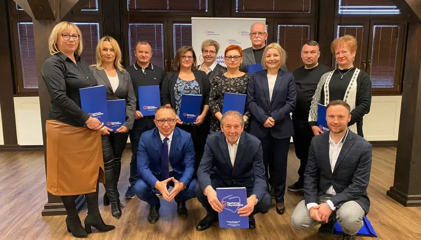 Grupa osób pozuje do zdjęcia z niebieskimi folderami. Na folderach widnieje napis "Platforma Obywatelska".