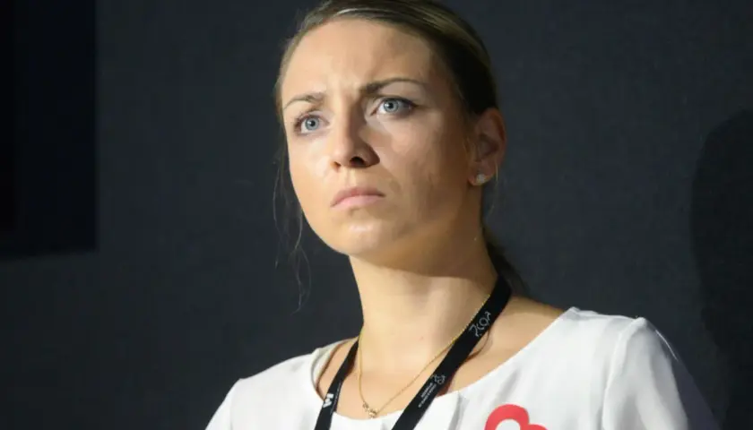 Posłanka Kinga Gajewska z zamyśloną miną, w białej bluzce z czerwonym sercem.