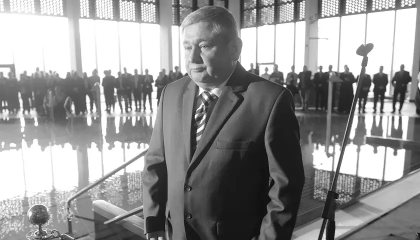 Jan Harhaj, starosta lidzbarski, w garniturze, stoi przed grupą ludzi w jasnym pomieszczeniu.