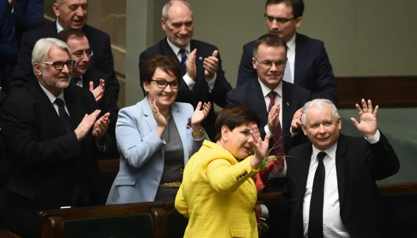 Kiedy rządził PiS, Beata Szydło w żółtej marynarce i Jarosław Kaczyński w garniturze pozdrawiają tłum.