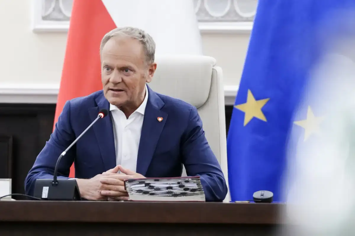 Donald Tusk w Sosnowcu, przemawia przy mikrofonie, za nim flagi Polski i UE.