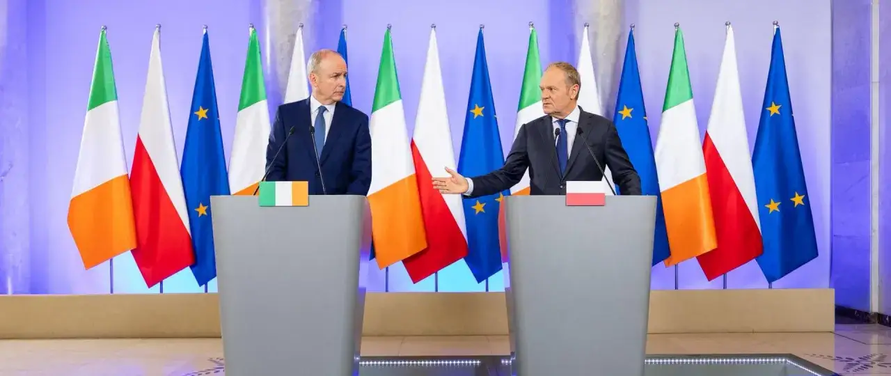 Dwóch polityków, jeden z flagą Irlandii, drugi z flagą Polski, przemawia na tle flag narodowych i UE. Może to być numer do TUSKA.