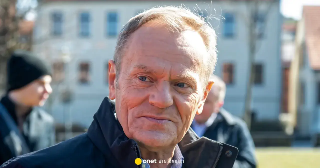 Zbliżenie na twarz Donalda Tuska. W tle widać niewyraźne sylwetki innych osób i budynki. Wiek Tuska jest tematem dyskusji, ale jego doświadczenie jest niezaprzeczalne.