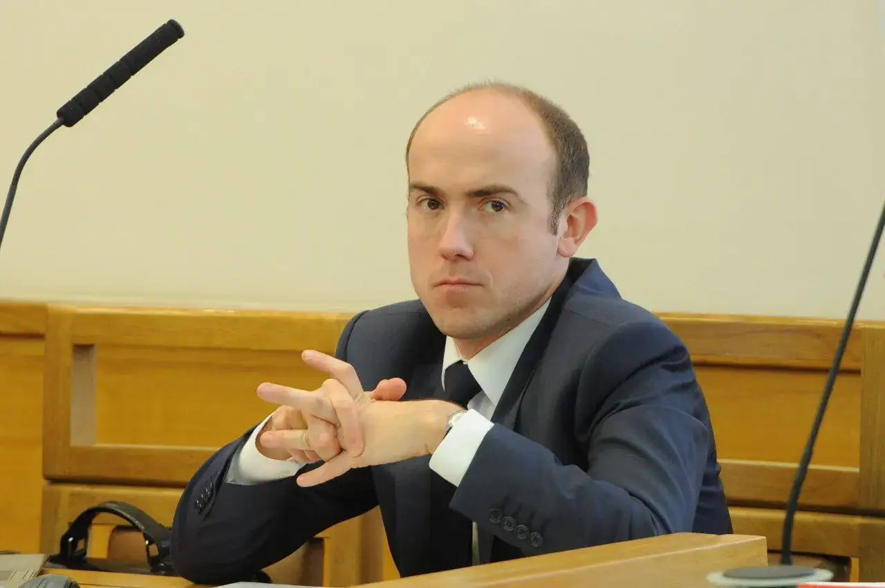 Borys Budka, polityk, w garniturze, z rękami splecionymi na stole. Wiek nie jest widoczny, ale jego postawa sugeruje skupienie.