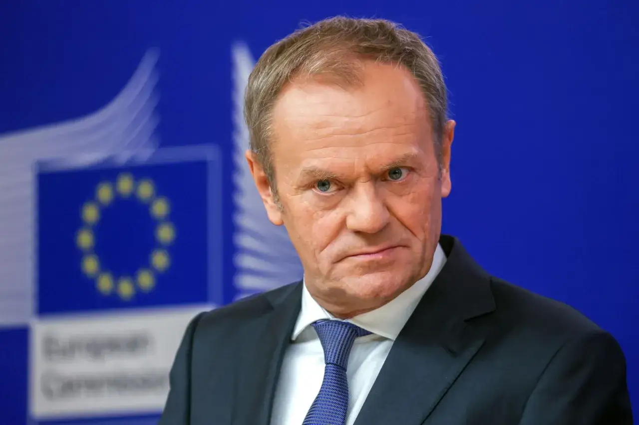 Donald Tusk w Brukseli, na tle niebieskiej ściany z logo Unii Europejskiej.