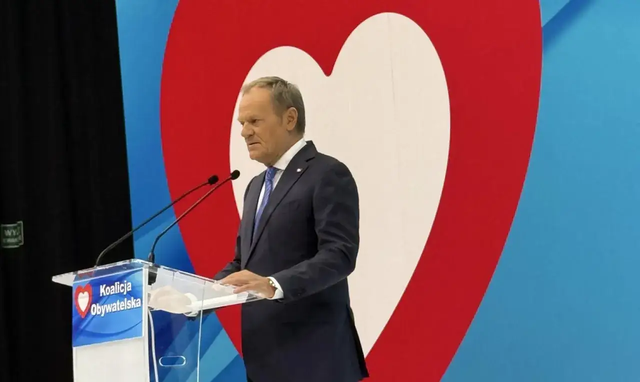 Donald Tusk przemawia na tle serca i logo Koalicji Obywatelskiej.