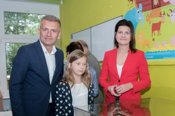 Bartosz Arłukowicz z córką i koleżanką na tle kolorowej ściany z bajkowymi zwierzątkami.