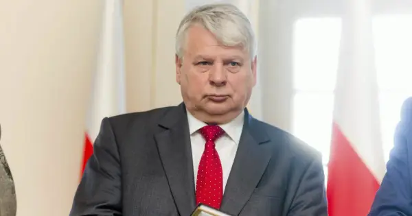 Bogdan Borusewicz w garniturze i czerwonym krawacie, na tle flagi Polski.