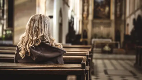 Kobieta z blond włosami siedzi w kościele, odwrócona tyłem. Obraz ilustruje badanie CBOS praktyki religijne.